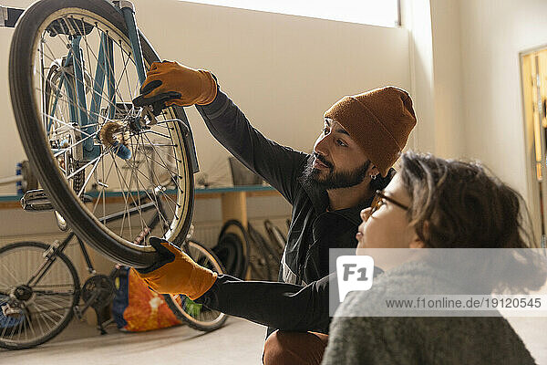 Männlicher Techniker zieht das Fahrradrad eines Jungen im Recyclingzentrum fest