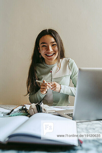 Porträt einer fröhlichen jungen Frau  die am Tisch Hausaufgaben macht