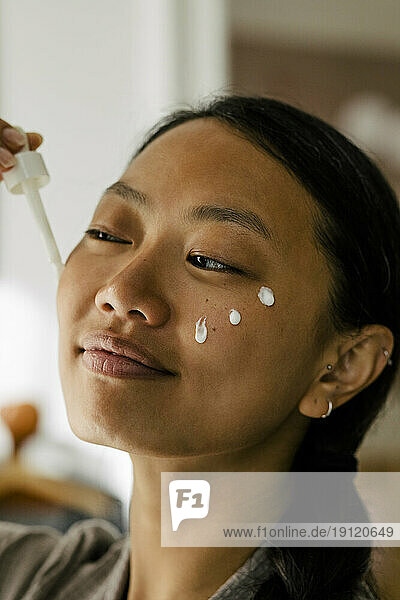 Smiling woman applying cream on face
