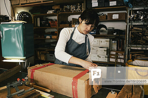 Unternehmerin beim Öffnen eines Kartons in einer Werkstatt