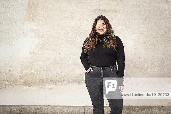 Porträt einer glücklichen Frau  die mit der Hand in der Tasche an der Wand eines Recyclingzentrums steht