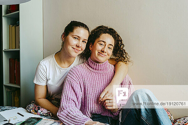 Porträt einer lächelnden jungen Frau mit einem Arm um einen Freund  der zu Hause sitzt