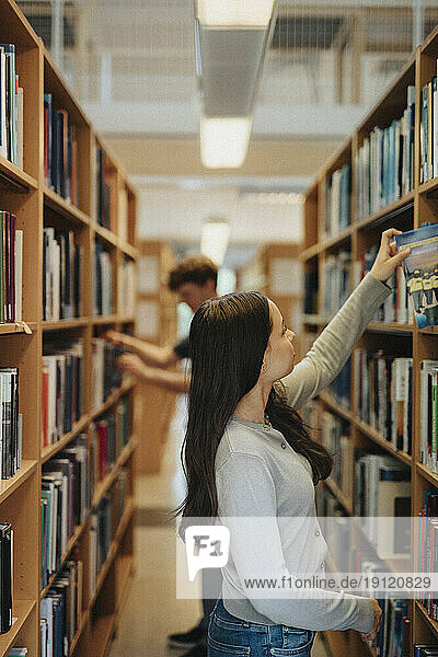 Seitenansicht einer Studentin  die in der Bibliothek der Universität Bücher im Regal sucht