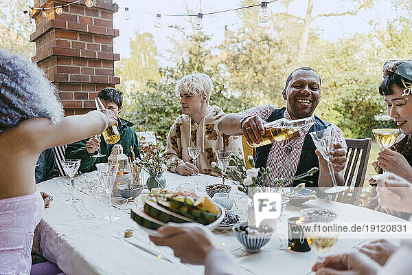 Glückliche Freunde aus der LGBTQ-Gemeinschaft trinken Wein  während sie bei einer Dinnerparty im Hinterhof am Tisch sitzen