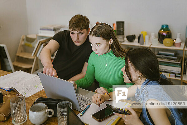 Junge Freunde erledigen gemeinsam Schulaufgaben  während sie zu Hause einen Laptop benutzen