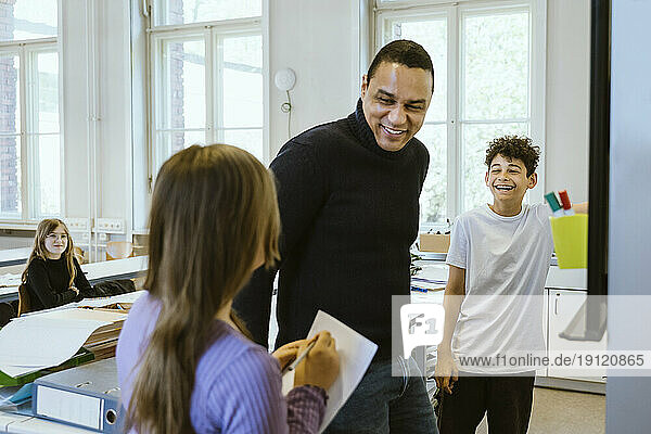 Glücklicher männlicher Lehrer  der sich mit den Schülern amüsiert  während er im Klassenzimmer unterrichtet