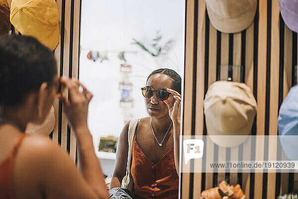 Frau probiert eine Sonnenbrille an  während sie ihr Spiegelbild in einer Modeboutique betrachtet