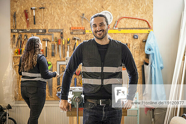 Porträt eines glücklichen männlichen Technikers  der sich auf einen Tisch im Recyclingzentrum stützt