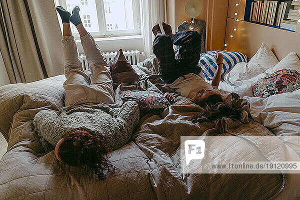 Playful female friends having fun while lying on bed at home