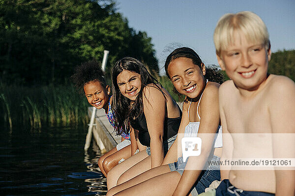 Portrait of happy children sitting together on jetty by lake at summer camp