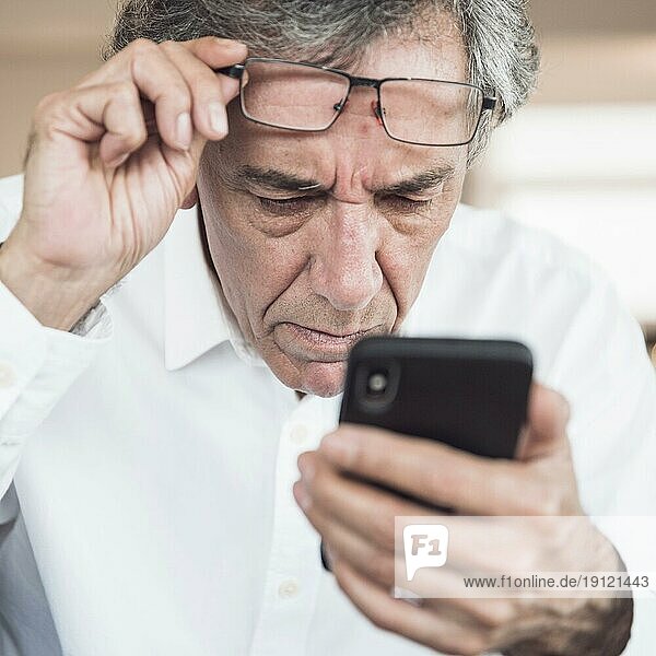 Nahaufnahme ernster älterer Mann  der auf sein Smartphone schaut