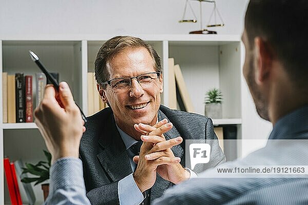 Porträt reifer glücklicher Anwalt mit Klient sitzend