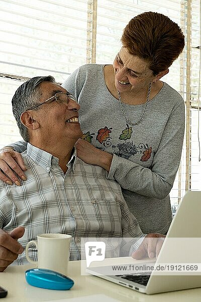Fröhliches reifes Paar  das zu Hause einen Laptop benutzt
