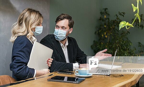 Geschäftsmann und Frau sprechen über ein neues Projekt  während sie medizinische Masken tragen