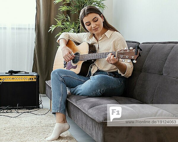 Seitenansicht weibliche Musikerin zu Hause spielen akustische Gitarre beim Sitzen Sofa