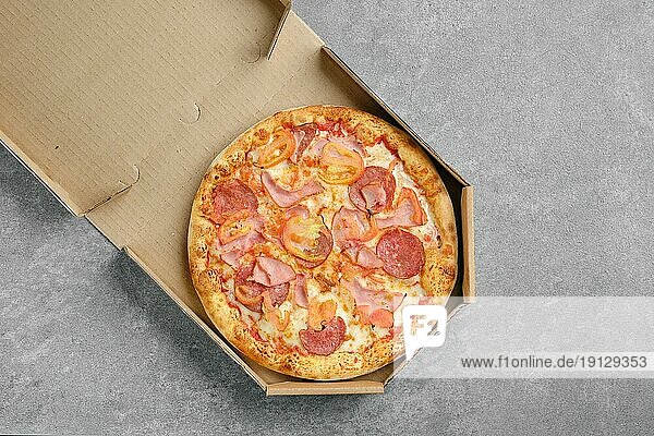 Draufsicht auf eine Pizza mit Schinken  Rohwurst und Tomatenscheiben im Karton