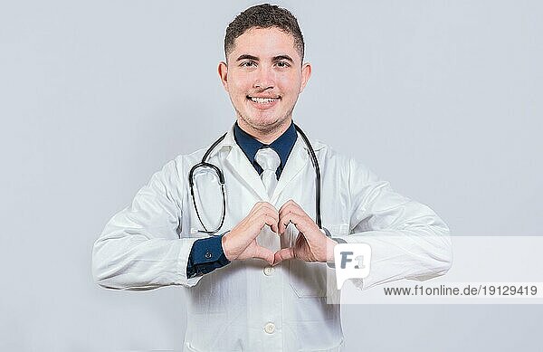 Freundlicher Arzt macht Herzgeste mit Händen isoliert. Junge lateinische Arzt macht Herzform auf isolierten Hintergrund