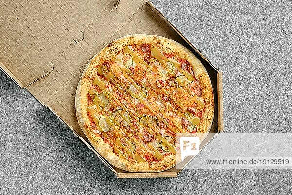 Draufsicht auf eine Pizza mit dünner Wurst und Essiggurke im Karton