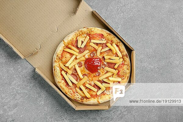 Draufsicht auf eine Pizza mit verschiedenen Würsten und Pommes frites in einer Pappschachtel