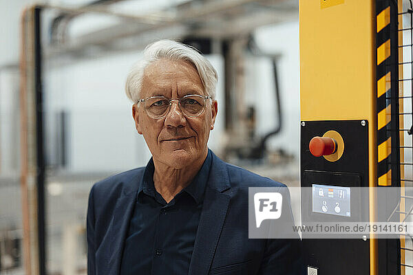 Smiling senior businessman wearing eyeglasses sanding in factory