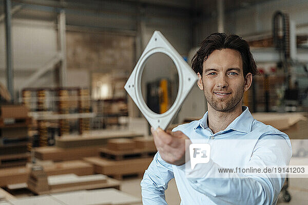 Smiling businessman with machine part in industry