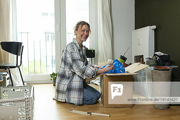Smiling young woman unpacking cardboard box at home