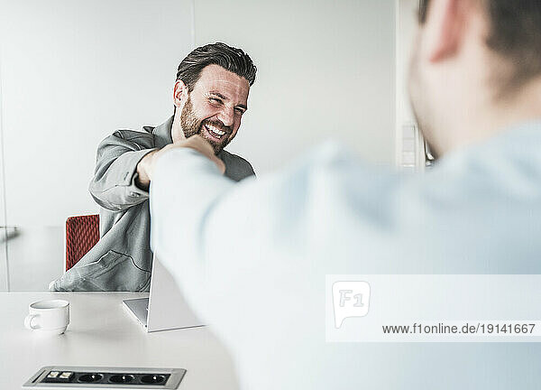 Happy businessman giving fist bump to colleague at office