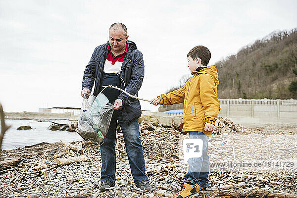 Father holding bag and son picking garbage at beach