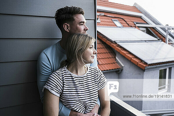 Smiling young couple leaning on wall on balcony