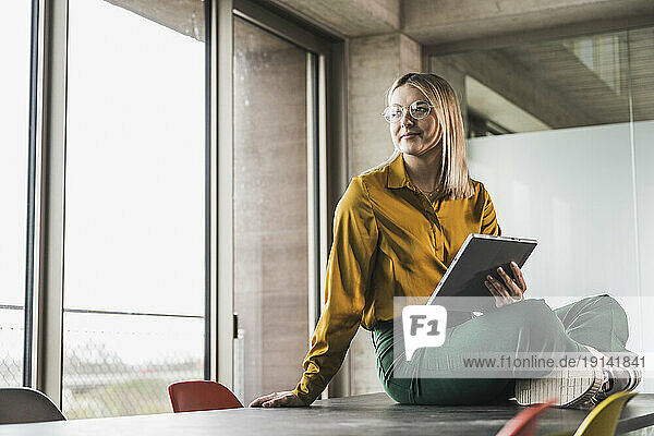 Contemplative businesswoman with tablet PC sitting on table at office