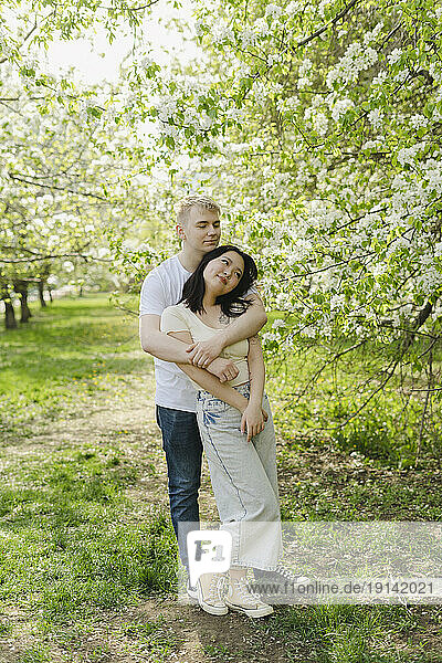 Young romantic couple embracing by tree in bloom at park