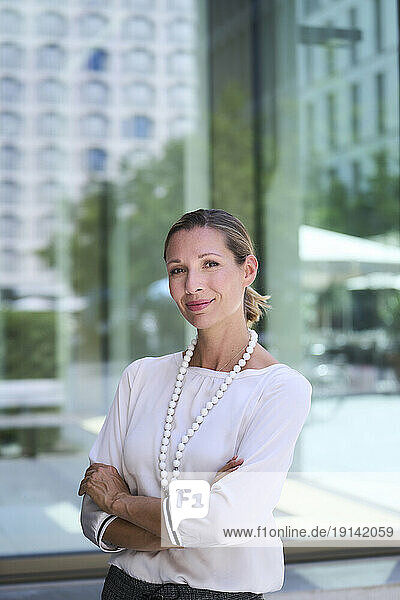 Confident businesswoman with arms crossed in front of glass wall