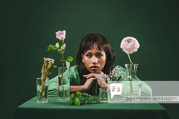Woman leaning on table with flowers in front of green backdrop