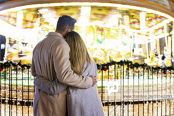 Couple hugging each other in front of carousel at Christmas market