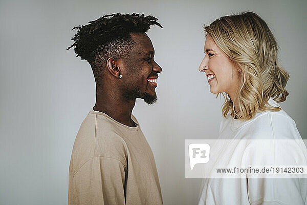 Smiling young woman looking at boyfriend against gray background