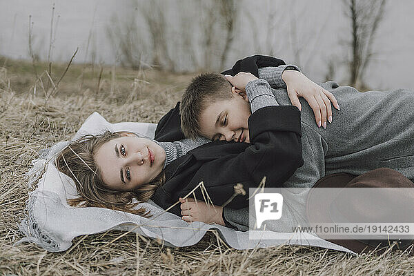 Mother embracing son lying on grassy field