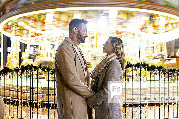Couple holding hands and standing in front of carousel at Christmas market