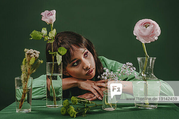 Thoughtful woman leaning on table with flowers in front of green backdrop