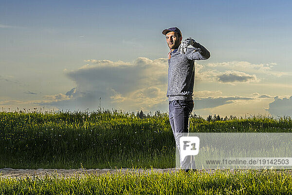 Man with golf club standing on grass at dusk