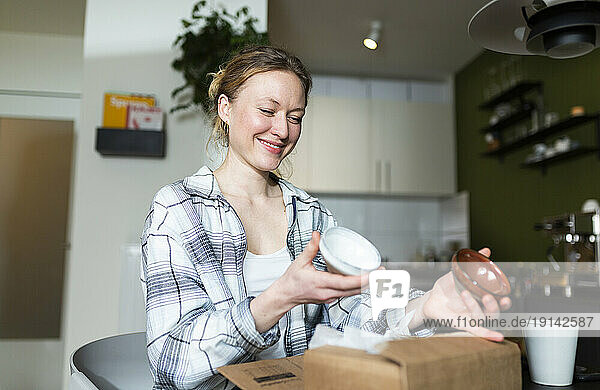 Smiling young woman unpacking ceramic bowls from cardboard box