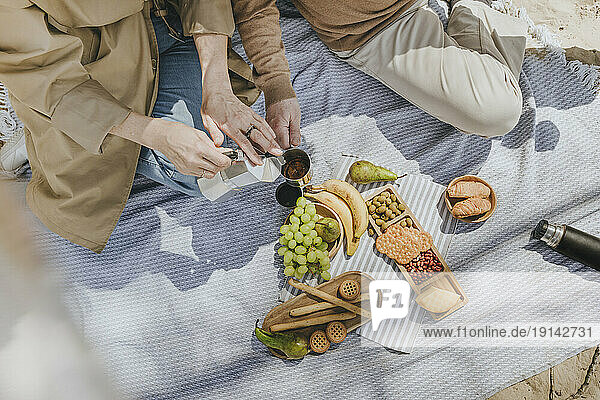 Couple enjoying coffee sitting on picnic blanket