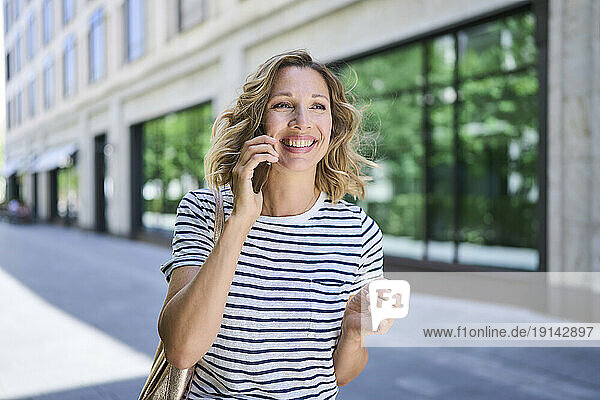 Happy blond woman talking on mobile phone near building