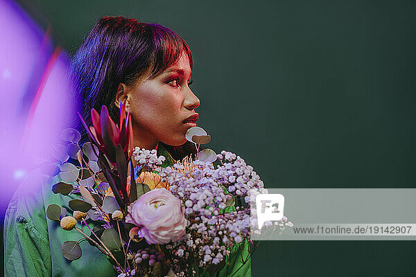 Young woman with flowers and neon lights in front of green backdrop