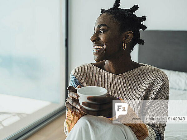 Smiling woman sitting on bed holding coffee cup