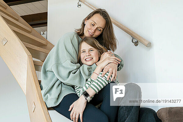 Mother embracing daughter sitting on steps at home
