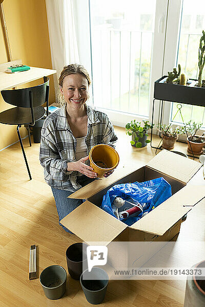 Smiling woman holding container by cardboard box at home