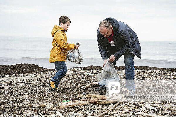 Father and son collecting garbage in bag at beach