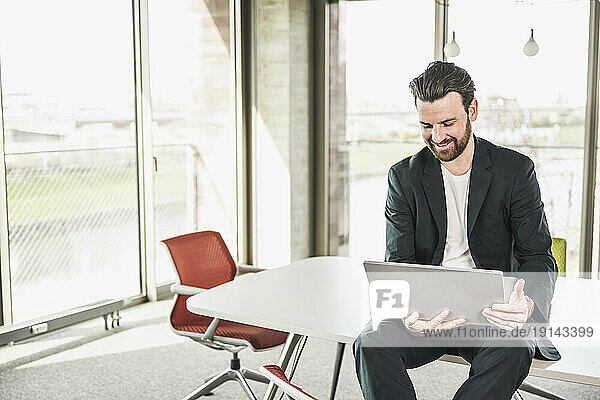 Smiling businessman sitting with laptop on table in office