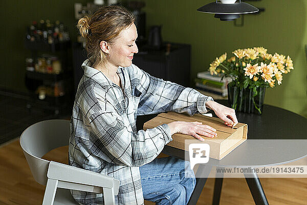 Young woman unpacking cardboard box on table