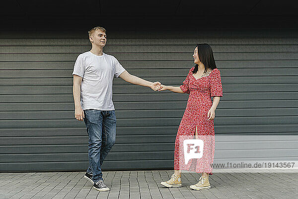 Romantic young couple holding hands in front of closed shutter